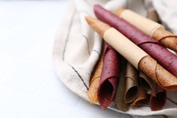 Tasty fruit leather rolls on white tiled table, closeup. Space for text