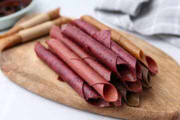 Tasty fruit leather rolls on white table, closeup