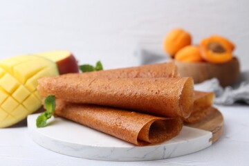 Delicious fruit leather rolls, mint, mango and apricots on white table, closeup