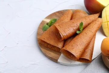 Delicious fruit leather rolls, mint and mango on white table, closeup. Space for text