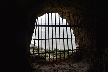 Ouverture dans une grotte offrant une vue sur la mer, fermée par une grille avec des barreaux en...