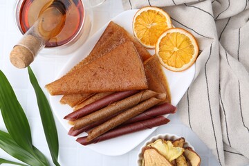 Tasty fruit leather rolls and orange slices on white table, flat lay