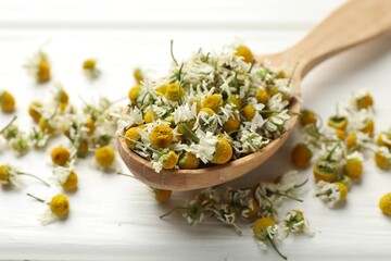 Dry chamomile flowers in spoon on white wooden table, closeup