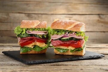 Tasty baguette sandwich with ham and vegetables on wooden table, closeup