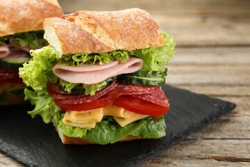 Tasty baguette sandwich with ham and vegetables on wooden table, closeup