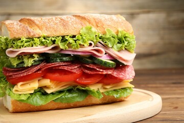 Tasty baguette sandwich with ham and vegetables on wooden table, closeup