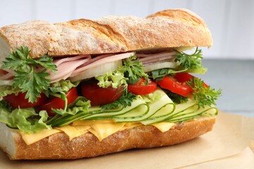 Tasty baguette sandwich with ham, cheese and vegetables on grey table, closeup