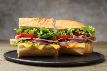 Pieces of tasty baguette sandwich with ham, cheese and vegetables on wooden table against grey background, closeup
