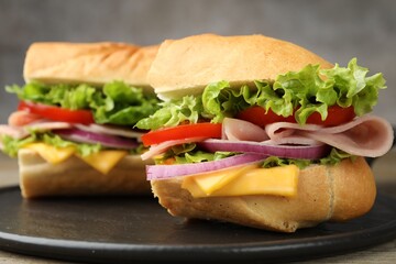 Pieces of tasty baguette sandwich with ham, cheese and vegetables on wooden table against grey...