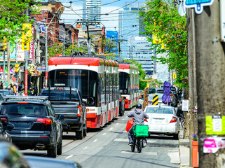 Fototapeta premium Gig economy: food delivery driver on aan electric bike in busy traffic with cars and light rail street cars shot on a sunny day in Toronto's Queen West district in summer