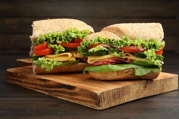 Pieces of tasty baguette sandwich with smoked sausage, cheese and vegetables on wooden table, closeup