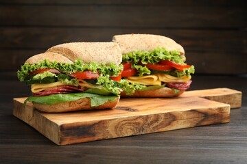 Pieces of tasty baguette sandwich with smoked sausage, cheese and vegetables on wooden table, closeup