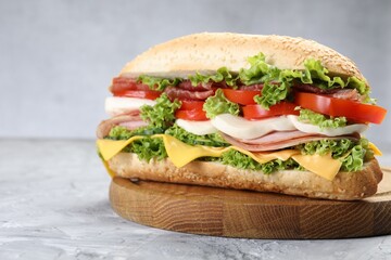 Tasty baguette sandwich with ham, cheese and vegetables on grey textured table, closeup