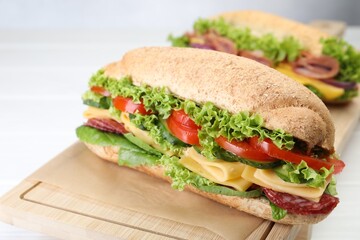 Tasty baguette sandwiches with smoked sausage, cheese and vegetables on white table, closeup