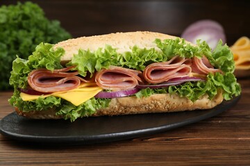 Tasty baguette sandwich with ham, cheese and vegetables on wooden table against dark background,...