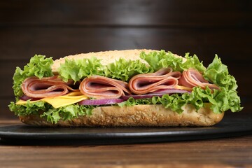 Tasty baguette sandwich with ham, cheese and vegetables on wooden table against brown background,...