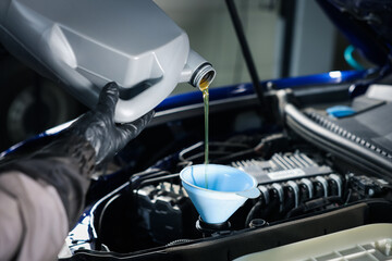 Worker pouring motor oil from canister into car engine, closeup