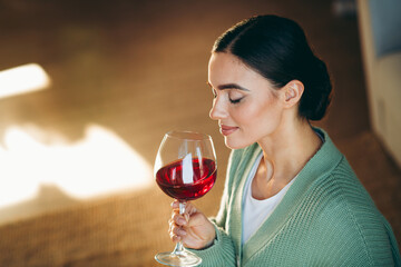 Young woman savoring a glass of red wine at home in a cozy living space with soft natural daylight
