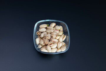 A glass bowl filled with roasted pistachios on a dark background. Healthy snack and nutritious food concept, minimalistic composition.