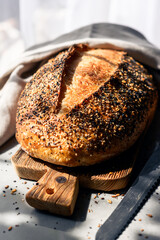Crispy sourdough bread with cracked crust and rugged texture, covered with different grains and wrapped in a linen towel. Artisan farmhouse-style loaf close up
