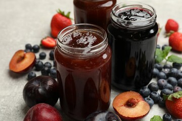 Different sweet jams in jars and ingredients on grey table, closeup