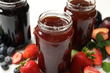 Different sweet jams in jars and ingredients on table, closeup