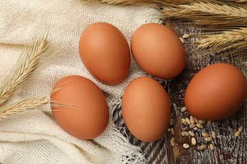 Raw eggs, fabric and spikes of wheat on wooden table, flat lay