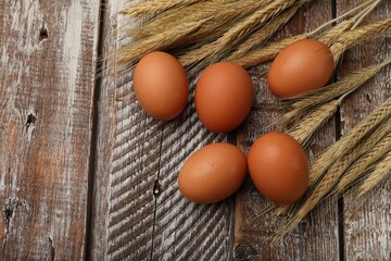 Raw eggs and spikes of wheat on wooden table, flat lay. Space for text