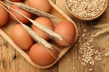 Fresh eggs, grains and spikes on wooden table, flat lay