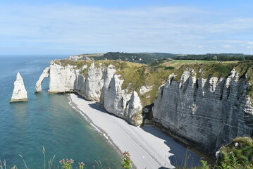 Plage et falaises d'Étretat, avec un rocher dans l'eau en forme de dent de requin.