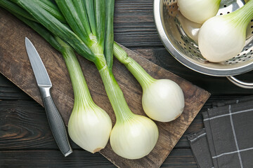 Fresh ripe green onions with cutting board and knife on black wooden table, flat lay