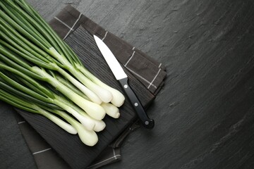 Fresh ripe green onions with cutting board and knife on black table, flat lay. Space for text