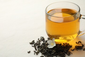 Aromatic jasmine tea in glass cup, flower and dried leaves on white table, closeup. Space for text