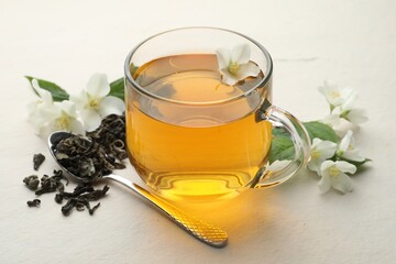 Aromatic jasmine tea in glass cup, flowers and leaves on white table, closeup