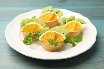 Tartlets with fruits and mint on light blue wooden table, closeup. Delicious dessert