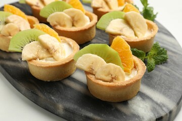 Tartlets with fruits and mint on white table, closeup. Delicious dessert