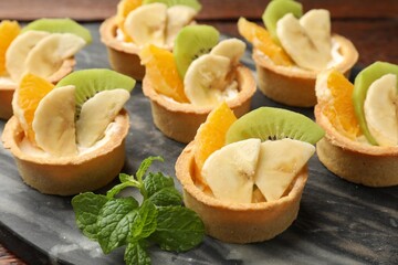 Tartlets with fruits and mint on table, closeup. Delicious dessert