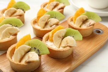 Tartlets with fruits on white table, closeup. Delicious dessert
