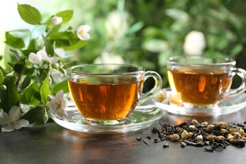 Aromatic jasmine tea in glass cups, brew and flowers on grey table outdoors, closeup