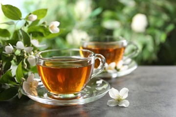 Aromatic jasmine tea in glass cups, flowers and green leaves on grey table outdoors, closeup. Space...