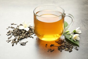 Aromatic jasmine tea in glass cup, brew and flowers on grey table, closeup