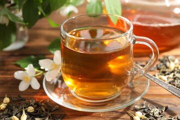 Aromatic jasmine tea in glass cup, brew and flowers on wooden table, closeup