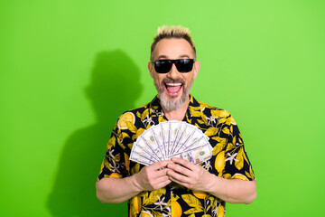 Charismatic man with dyed hair and summer shirt showing cash against green background, embodying happiness and excitement