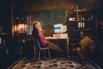 Elderly man using a vintage computer in a cozy home office setting, surrounded by organized bookshelves