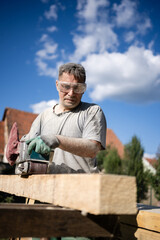 Carpenter sanding wooden beam outdoors on construction site