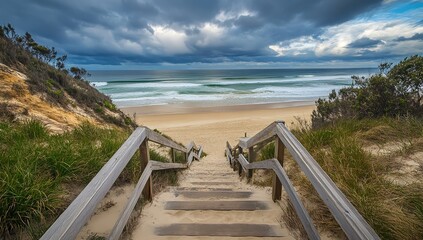 Wide-angle view of stairs descending toward a moody beach under a cloudy sky, with deep green and blue tones creating a dramatic coastal atmosphere
