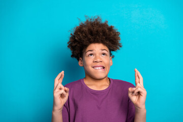 Smiling teenage boy crossing fingers for luck on blue background, cheerful and charming hope gesture for positive outcome © deagreez