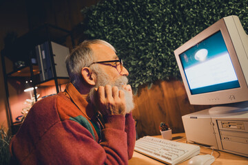 Elderly man working on an old computer in a cozy home office setting, embodying dedication