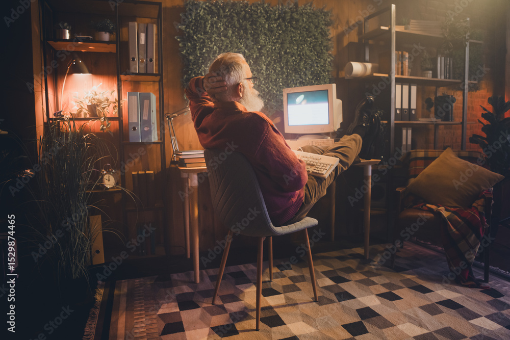 Poster elderly man working on a computer in a cozy home office, immersed in online programming and enjoying