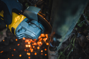 The hands of the master saw the metal with a grinder. Metal works in the workshop close up. Metal processing with angle grinder. Sparks in metalworking.